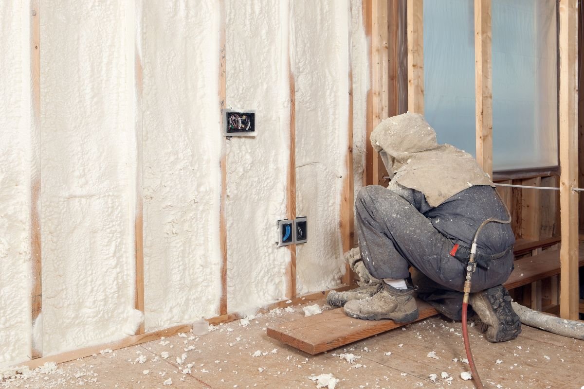 A man wearing a white jacket and hat is focused on working on a wall, using tools for construction or repair. 