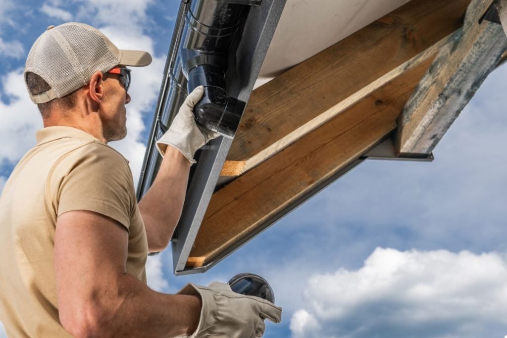 A man is positioned on a ladder, performing maintenance work on a roof while ensuring safety precautions.