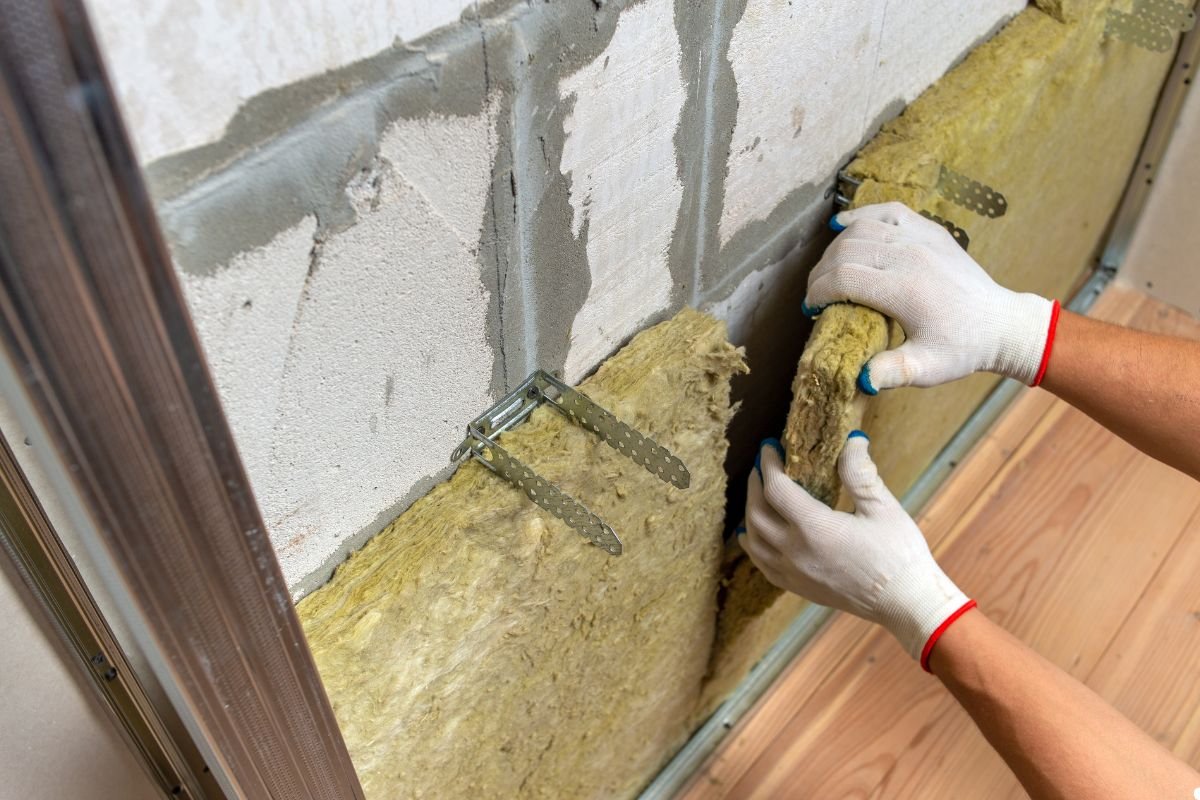 A person installs insulation material into a wall, wearing protective gear and focused on the task at hand.