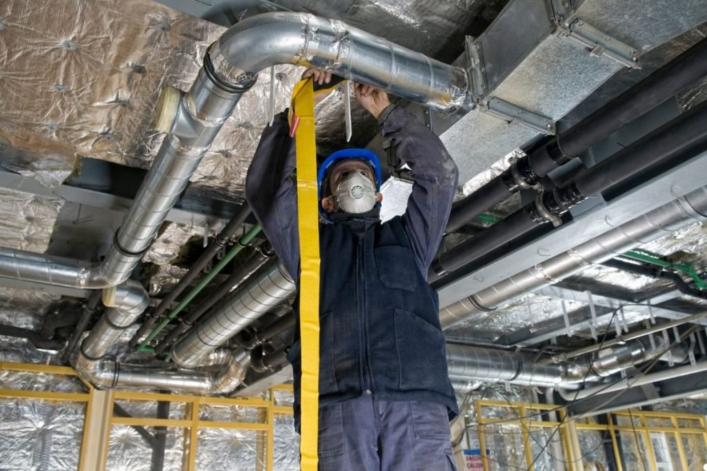A man wearing a safety mask and protective gear measures with a tape measure, focused on his task.
